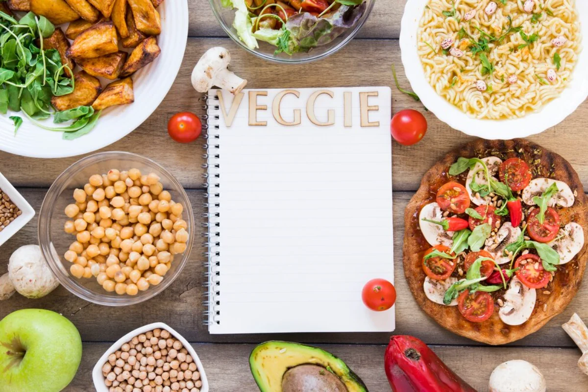 An overhead view of a vegetarian meal spread on a wooden table, featuring an open notebook labelled