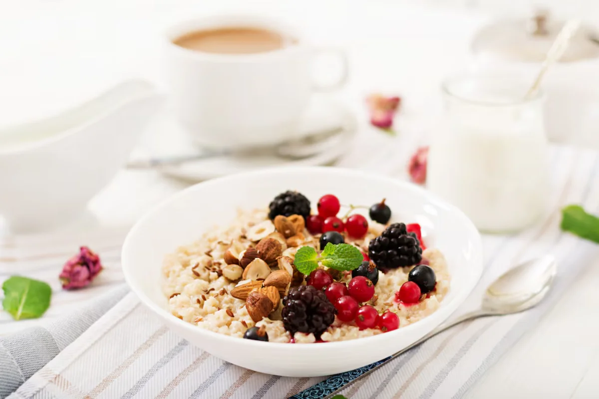 A healthy breakfast setup showing a bowl of oatmeal topped with fresh blackberries, red currants, and almonds