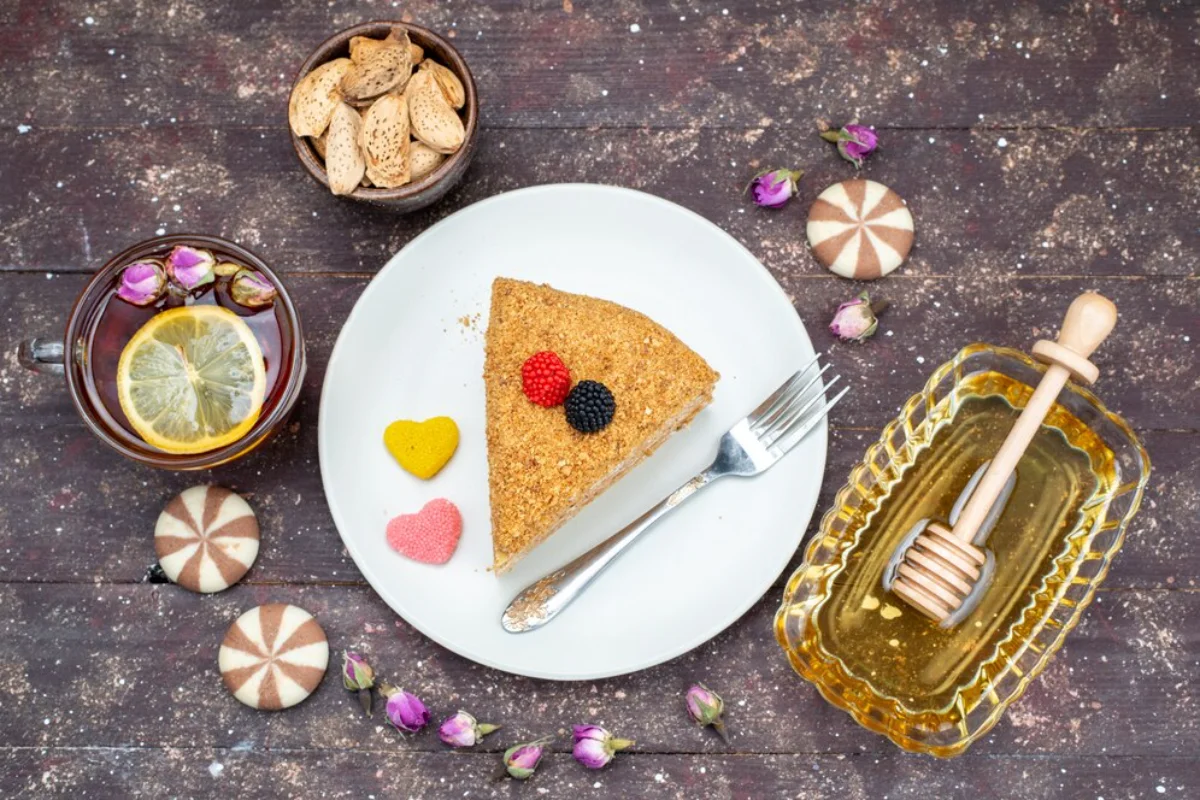 A charming tea time spread featuring a slice of nutty cake topped with fresh berries on a white plate, accompanied by a cup of tea with lemon