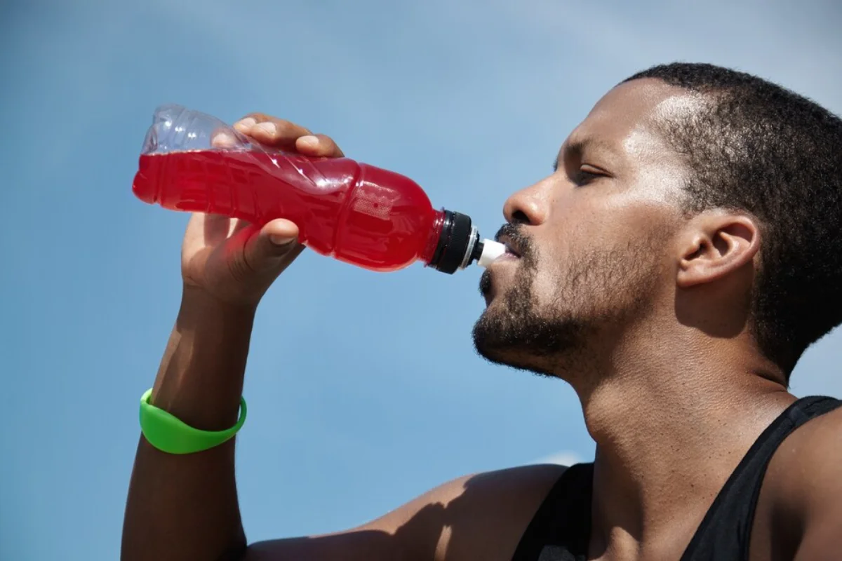 A man drinking from a bright red sports drink bottle