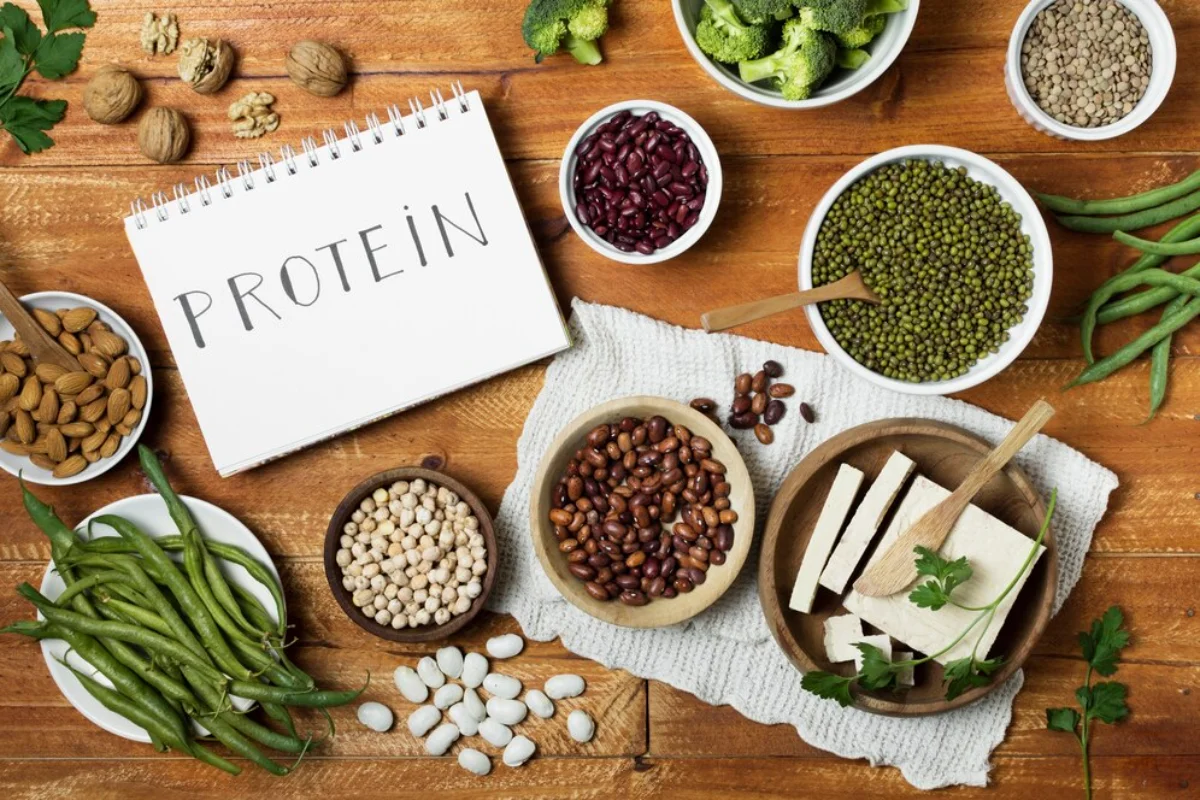 A variety of protein-rich foods displayed on a wooden table, including almonds, beans, tofu, mung beans, chickpeas