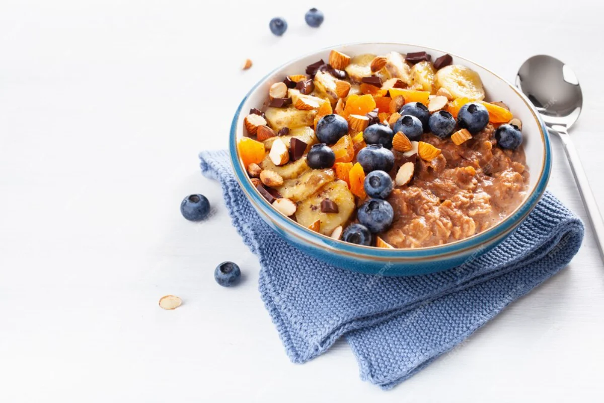 A bowl of oatmeal topped with blueberries, chopped almonds, diced apricots, and banana slices