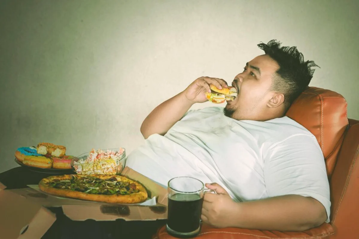 A man reclining on an orange sofa, eating a burger