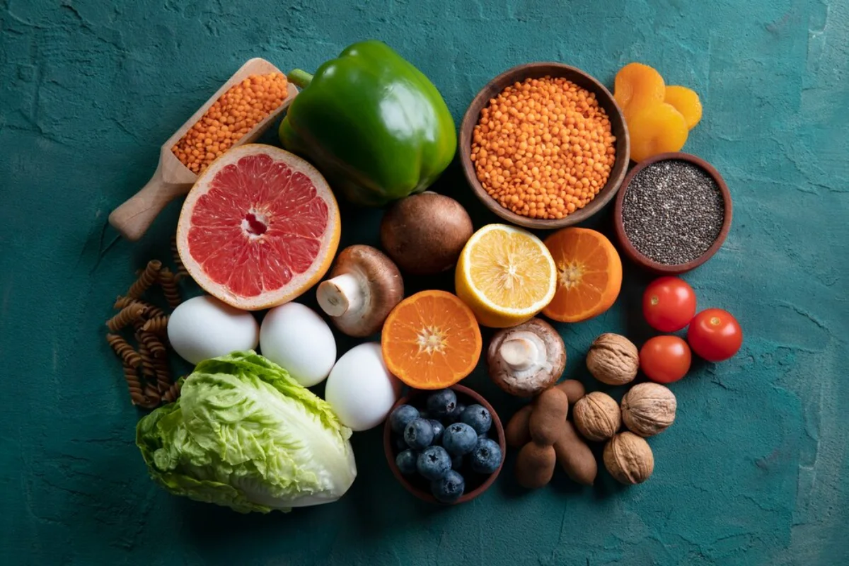 A variety of fresh fruits, vegetables, eggs, nuts, and legumes arranged on a textured turquoise surface