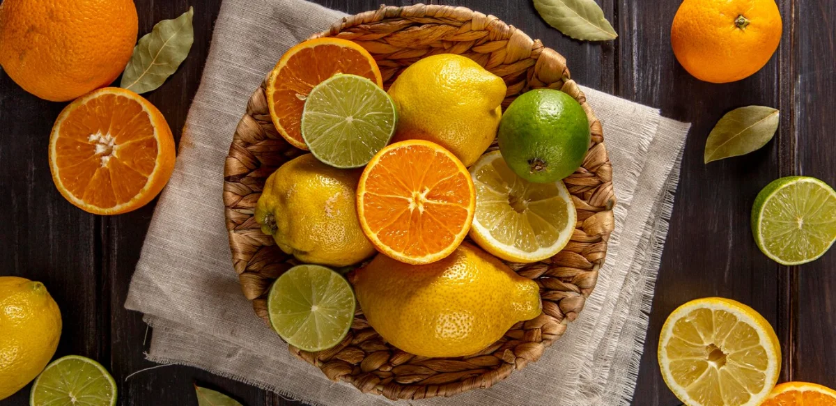 A variety of citrus fruits, including oranges, lemons, and limes, displayed in and around a rustic woven basket