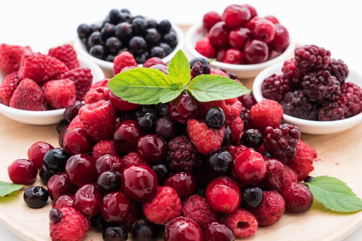 Assorted fresh berries including raspberries, blackberries, blueberries, and cherries on a wooden board