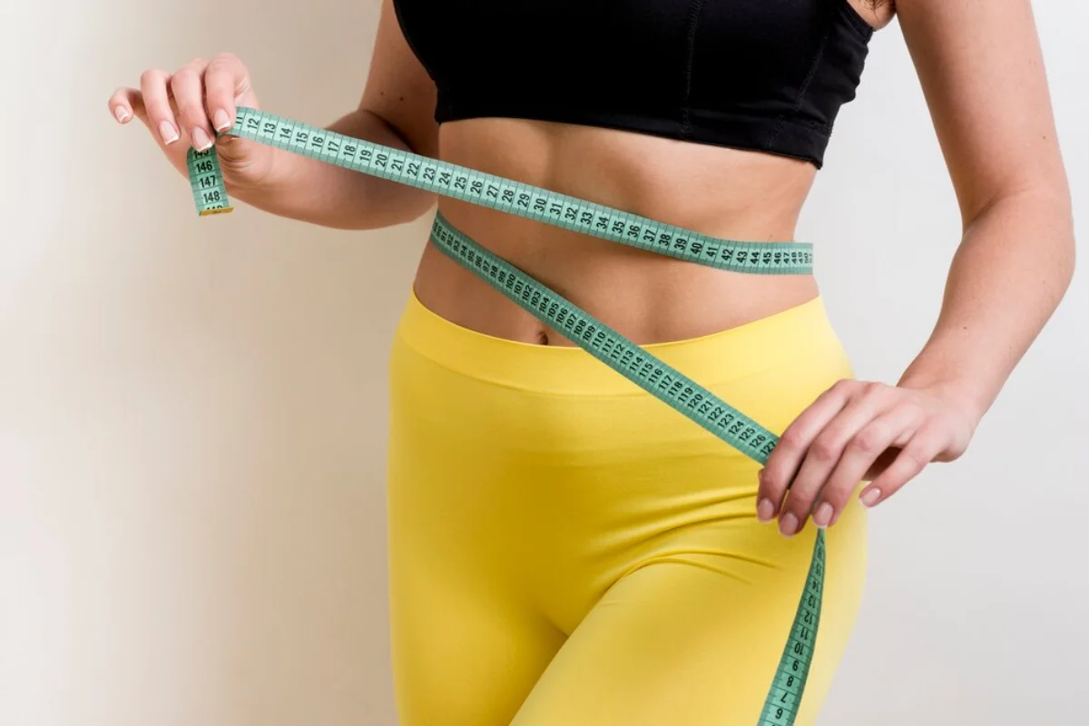 A woman in sportswear measures her waist with a tape measure.
