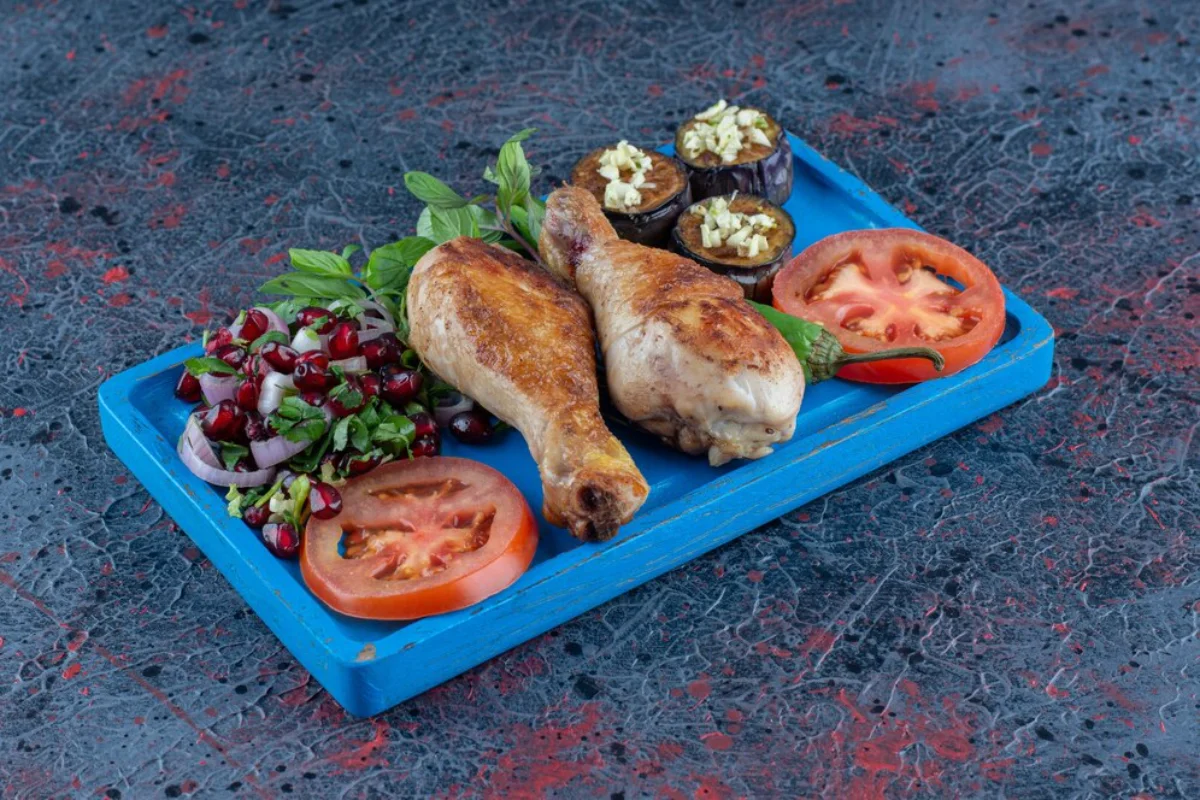 A vibrant dish of roasted chicken legs, grilled aubergines topped with garlic, fresh tomato slices