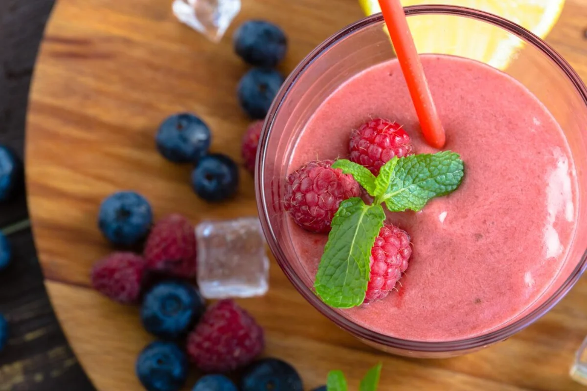 berry smoothie in a glass garnished with fresh raspberries and mint,