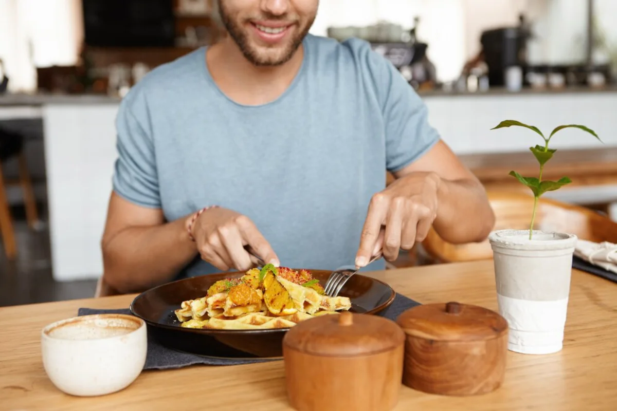 A man enjoying a meal of waffles topped with chicken and a sprinkle of herbs