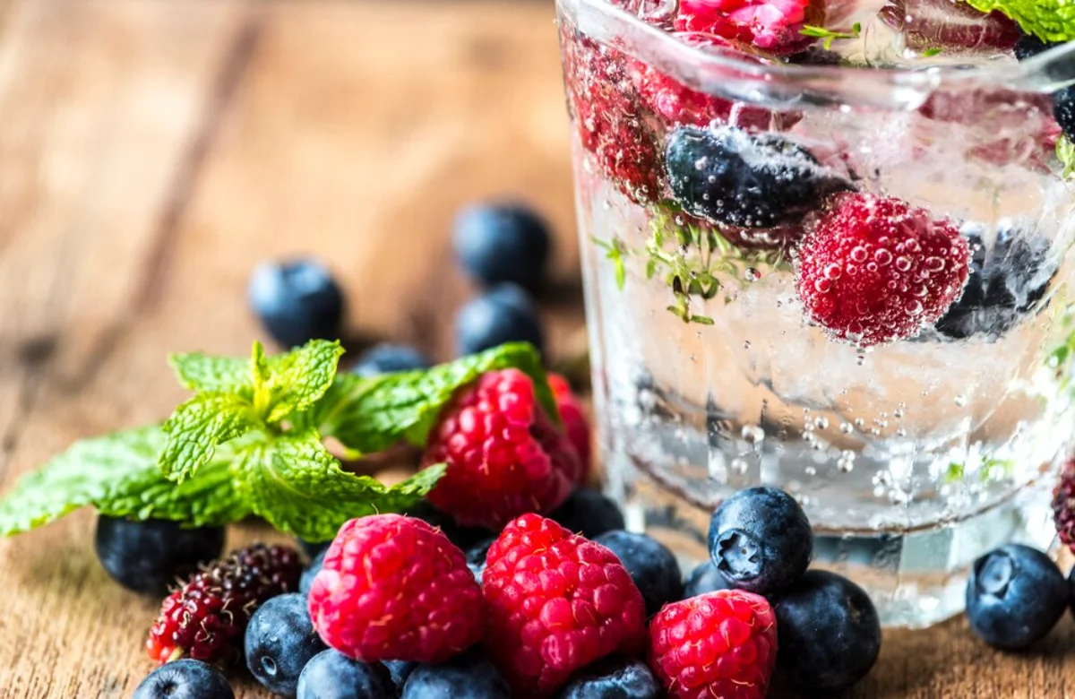 A refreshing glass of sparkling water filled with raspberries, blackberries, and blueberries, garnished with a sprig of mint