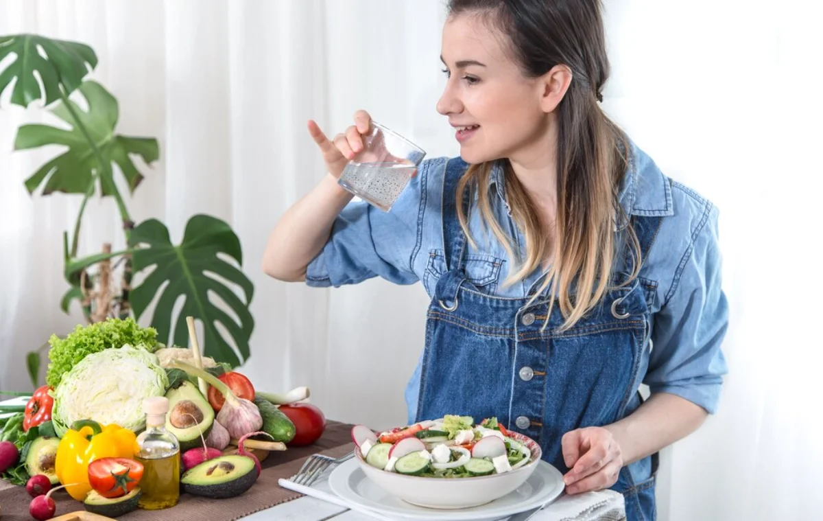 A woman in a denim jacket prepares to sprinkle chia seeds onto a fresh vegetable salad