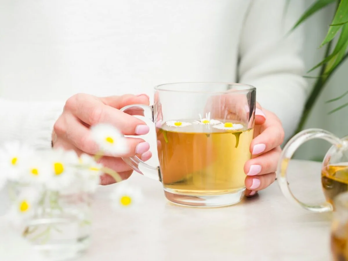 A person holding a clear glass cup of chamomile tea