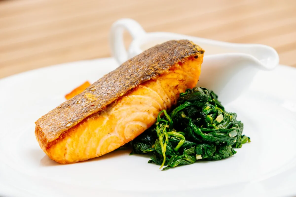 A plate of grilled salmon with crispy skin served alongside sautéed spinach, presented on a white dish