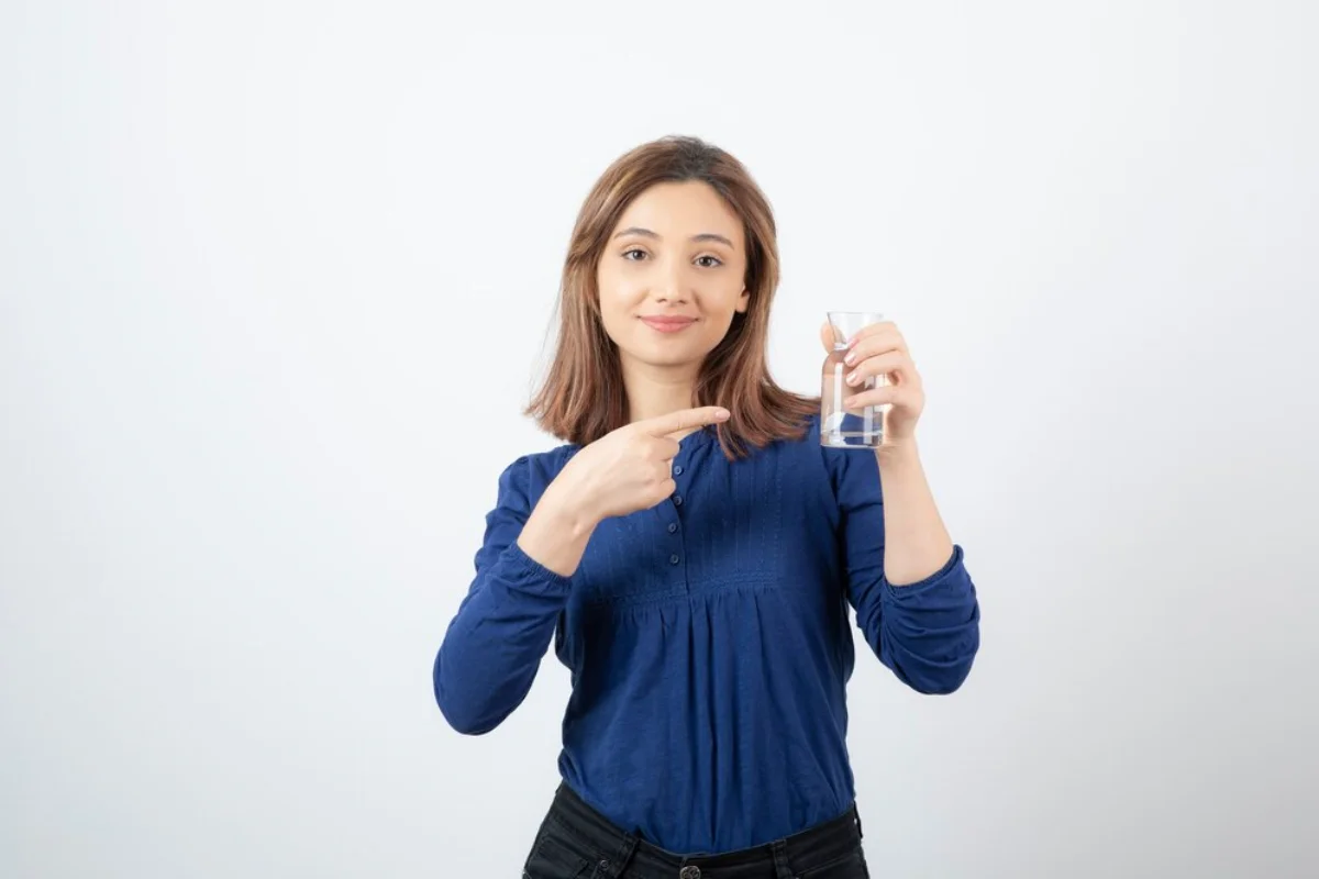 A young woman in a blue blouse pointing to a glass of water