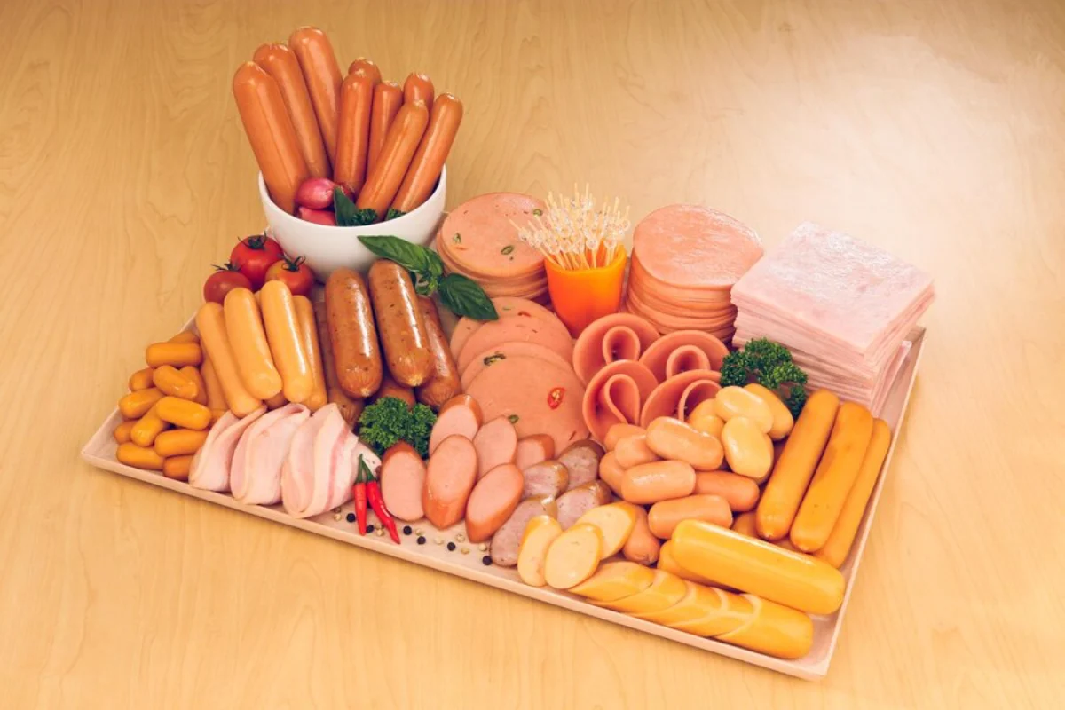 Assorted processed meats including sausages, hams, and cold cuts, artistically arranged on a platter with some garnishes like parsley and cherry tomatoes 