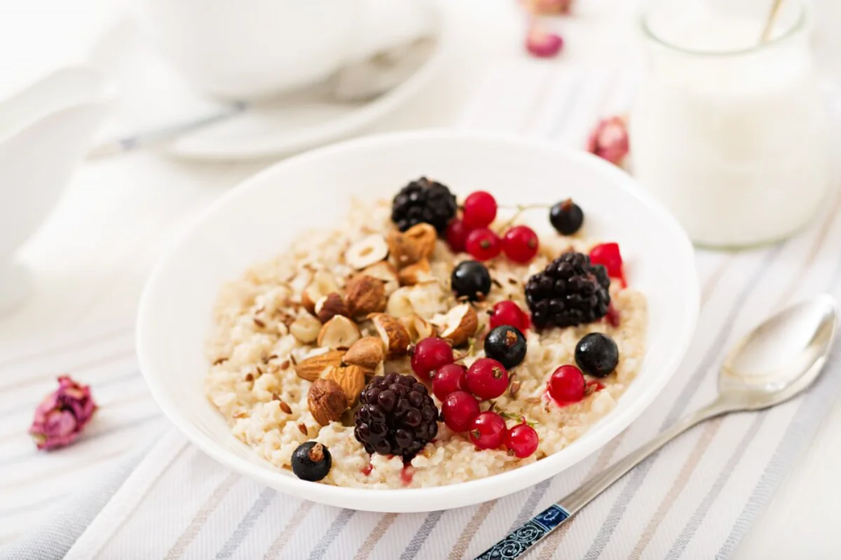 A bowl of oatmeal topped with fresh berries and nuts, accompanied by a glass of milk