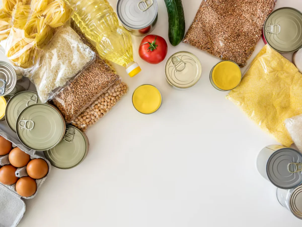 Assorted food supplies including canned goods, bags of grains, bottles of oil, and fresh vegetables
