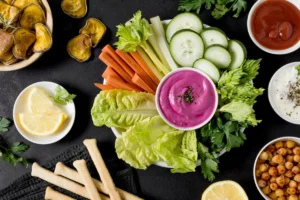 A vibrant assortment of healthy snacks featuring colourful vegetable sticks, such as carrots, celery, and cucumber, accompanied by various dips including beetroot hummus, yoghurt, and ketchup