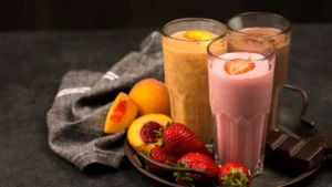 Three different fruit smoothies in tall glasses, garnished with slices of peach and strawberry