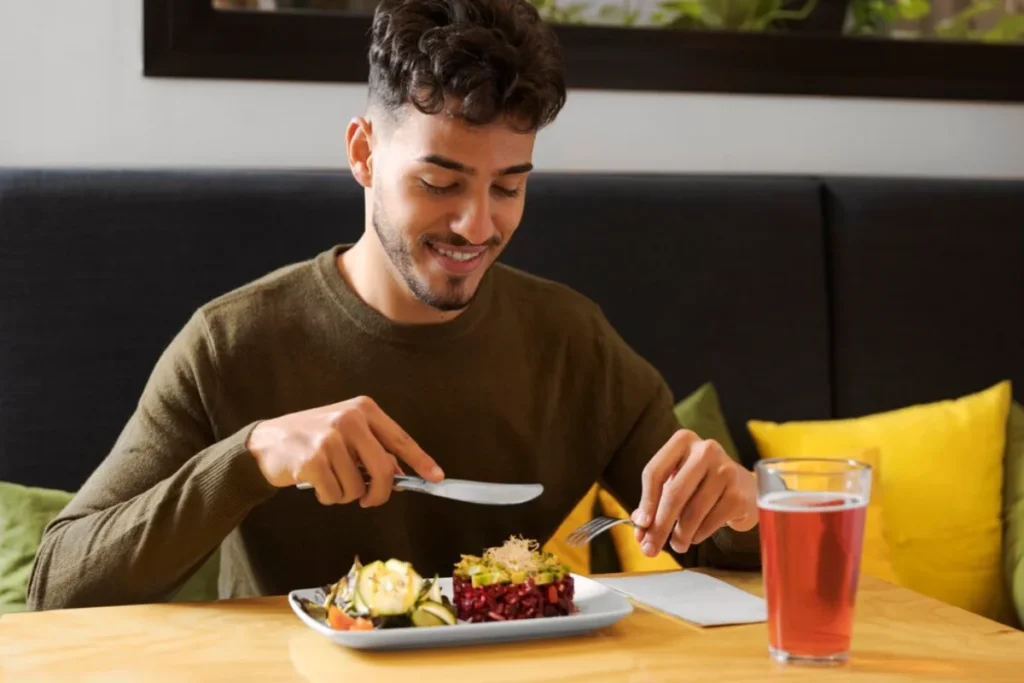 A young man smiling as he prepares to eat a healthy meal consisting of various vegetables and grains