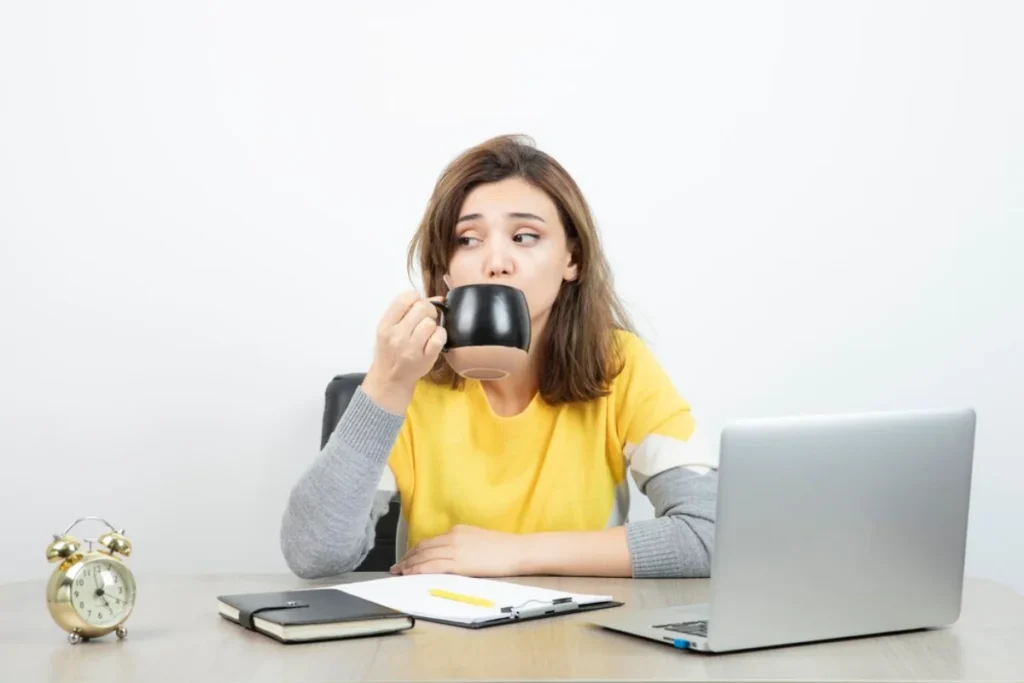 Young woman drinking from a mug while sitting at a desk with a laptop