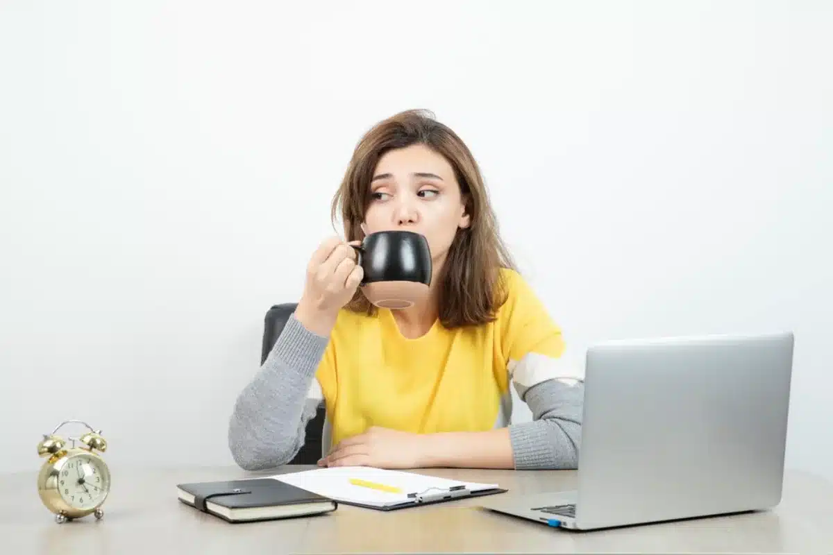 Young woman drinking from a mug while sitting at a desk with a laptop