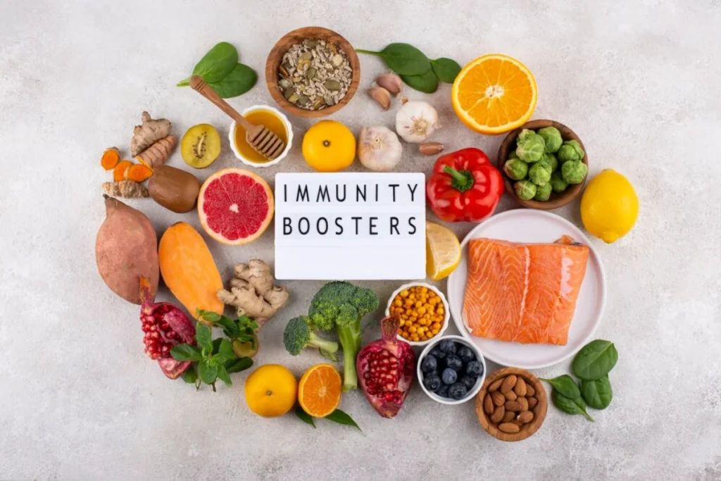 A variety of fresh fruits, vegetables, nuts, and salmon arranged around a sign that reads "Immunity Boosters