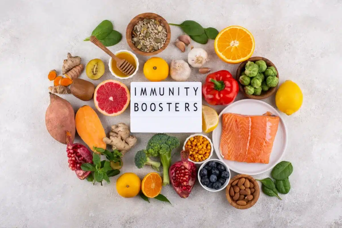 A variety of fresh fruits, vegetables, nuts, and salmon arranged around a sign that reads "Immunity Boosters