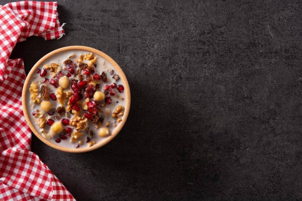 A wooden bowl filled with yogurt, granola, and pomegranate seeds, accompanied by a red and white checkered cloth.